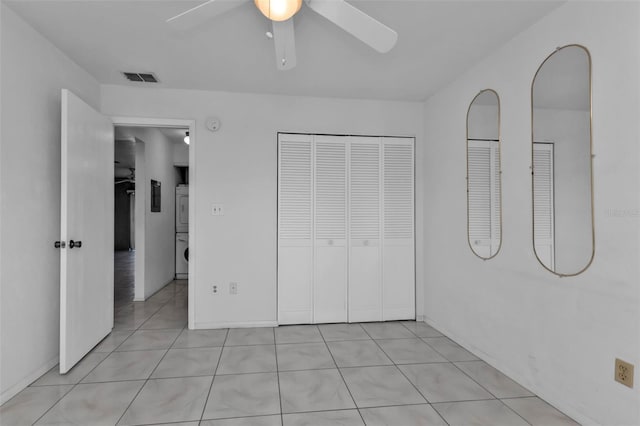 unfurnished bedroom featuring multiple closets, ceiling fan, light tile patterned flooring, and stacked washer and clothes dryer