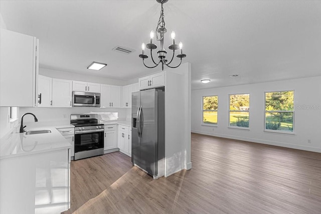 kitchen featuring light hardwood / wood-style floors, white cabinetry, pendant lighting, and appliances with stainless steel finishes