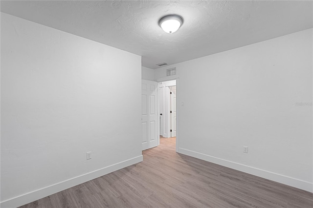 empty room with light hardwood / wood-style floors and a textured ceiling