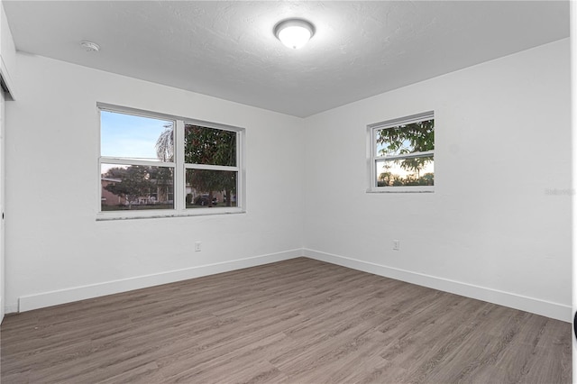 unfurnished room with a healthy amount of sunlight, a textured ceiling, and dark wood-type flooring