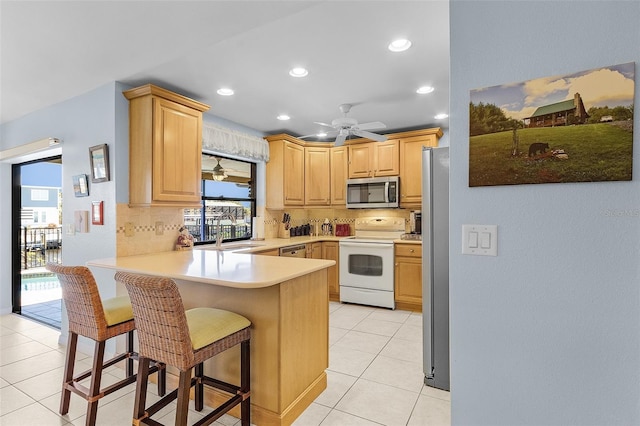 kitchen featuring a breakfast bar, backsplash, light brown cabinetry, kitchen peninsula, and stainless steel appliances