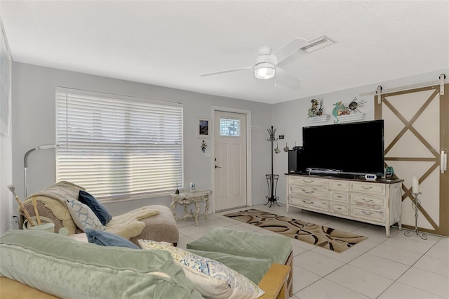 tiled living room with a barn door and ceiling fan