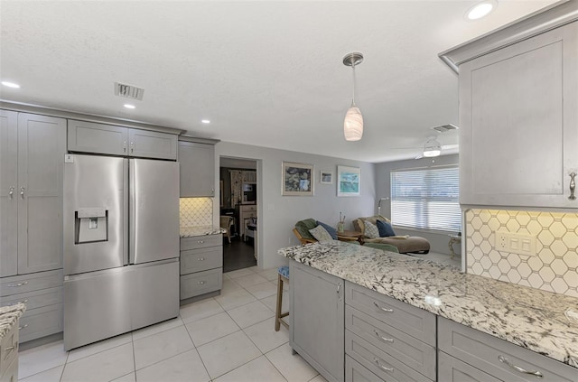 kitchen featuring gray cabinetry, tasteful backsplash, stainless steel fridge with ice dispenser, pendant lighting, and a breakfast bar area