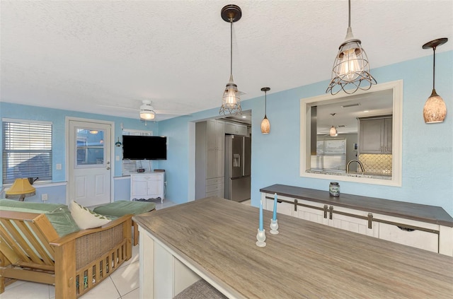 kitchen with stainless steel refrigerator with ice dispenser, hanging light fixtures, a textured ceiling, tasteful backsplash, and light tile patterned flooring