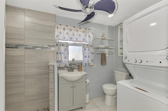 bathroom featuring ceiling fan, tile patterned flooring, toilet, vanity, and stacked washer and clothes dryer