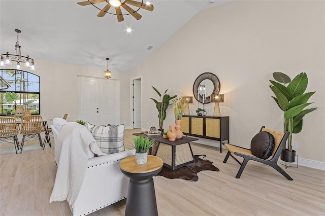 living area with lofted ceiling, light wood-type flooring, and ceiling fan with notable chandelier