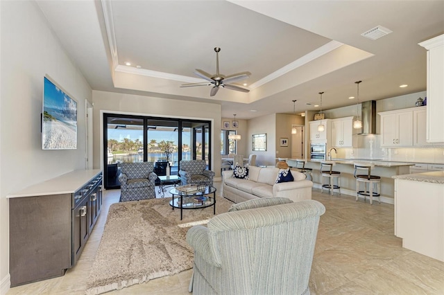 living room featuring a tray ceiling, ceiling fan, and crown molding