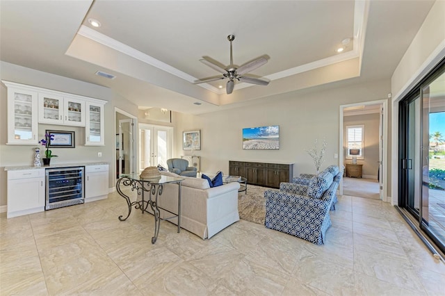 living room featuring french doors, wine cooler, indoor bar, ceiling fan, and a tray ceiling