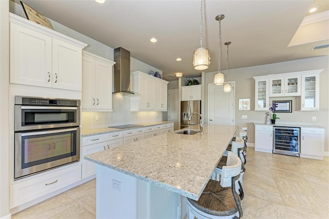 kitchen with appliances with stainless steel finishes, wall chimney exhaust hood, white cabinetry, and beverage cooler