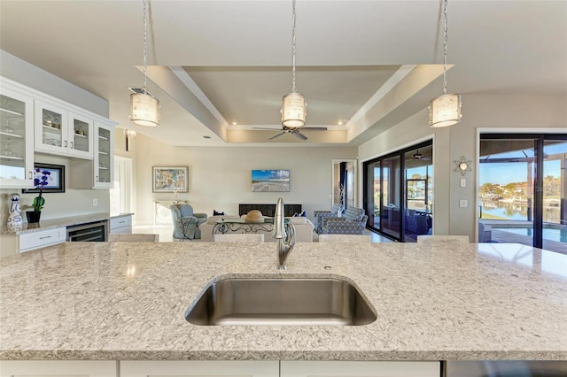 kitchen featuring a tray ceiling, sink, a water view, and hanging light fixtures