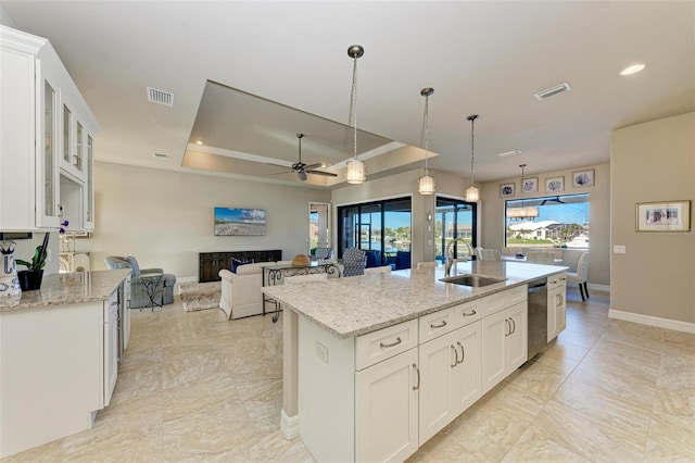 kitchen with white cabinetry, sink, ceiling fan, a tray ceiling, and a kitchen island with sink