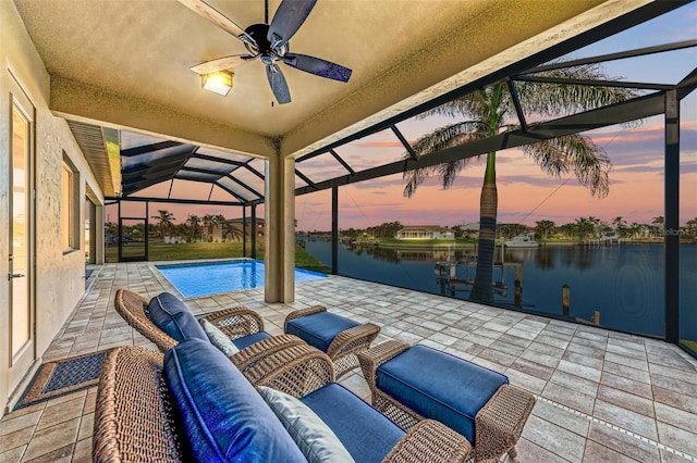 patio terrace at dusk with an outdoor living space, a water view, ceiling fan, and a lanai