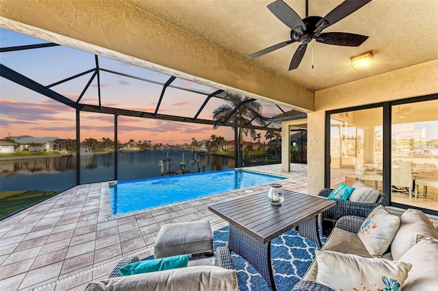 pool at dusk featuring glass enclosure, a patio area, a water view, and ceiling fan