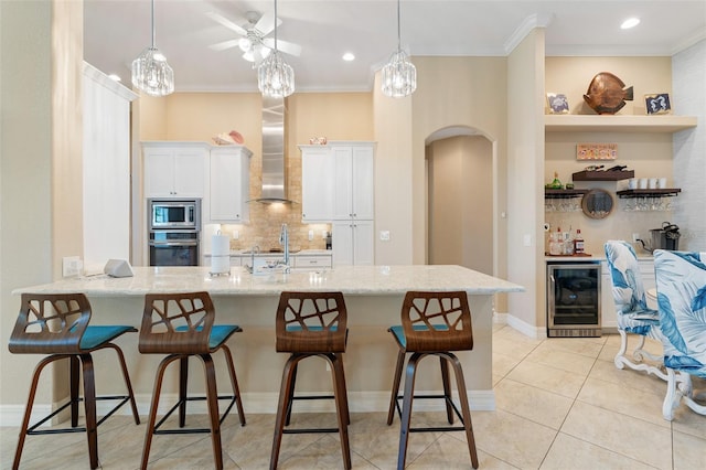 kitchen featuring a kitchen bar, appliances with stainless steel finishes, wall chimney range hood, white cabinetry, and wine cooler