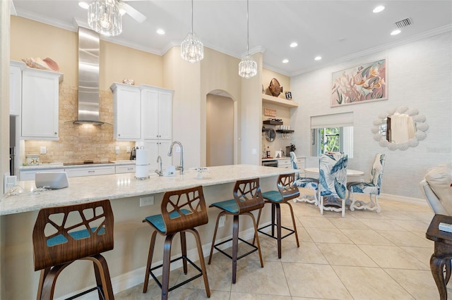 kitchen with a kitchen bar, pendant lighting, white cabinetry, and wall chimney range hood