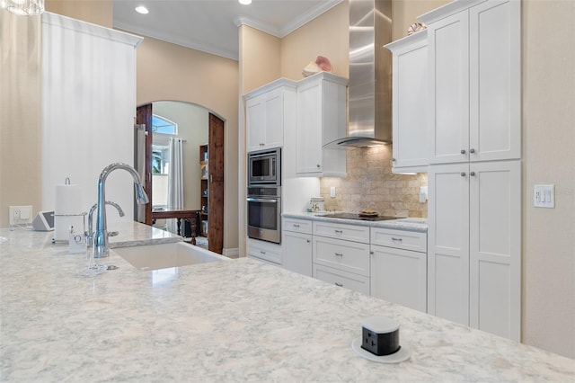 kitchen featuring white cabinetry, crown molding, stainless steel appliances, and wall chimney range hood