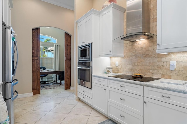 kitchen featuring white cabinetry, stainless steel appliances, wall chimney range hood, light stone counters, and light tile patterned flooring