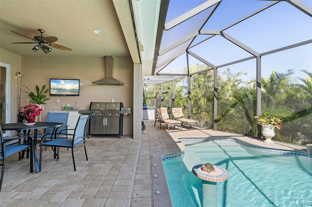 view of pool with glass enclosure, grilling area, an outdoor kitchen, ceiling fan, and a patio