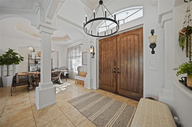 foyer entrance with decorative columns, ornamental molding, a notable chandelier, a high ceiling, and light tile patterned flooring