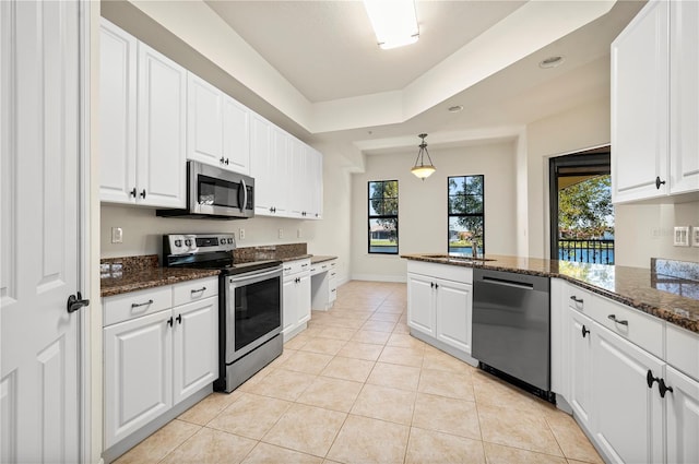 kitchen with stainless steel appliances, white cabinets, dark stone counters, decorative light fixtures, and light tile patterned flooring