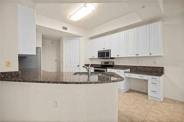 kitchen featuring white cabinetry, kitchen peninsula, stainless steel appliances, and dark stone counters