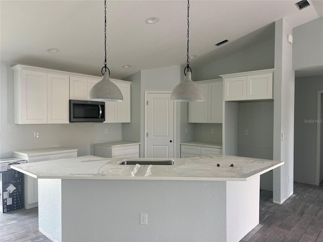 kitchen with hanging light fixtures, stainless steel microwave, a center island with sink, and white cabinetry