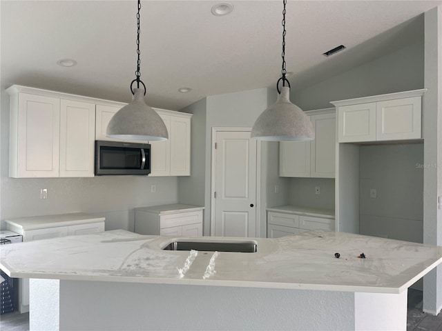 kitchen with stainless steel microwave, an island with sink, white cabinetry, and pendant lighting