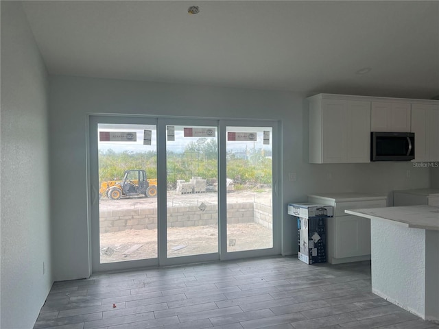 kitchen featuring a textured wall, light wood-style flooring, stainless steel microwave, light countertops, and white cabinetry