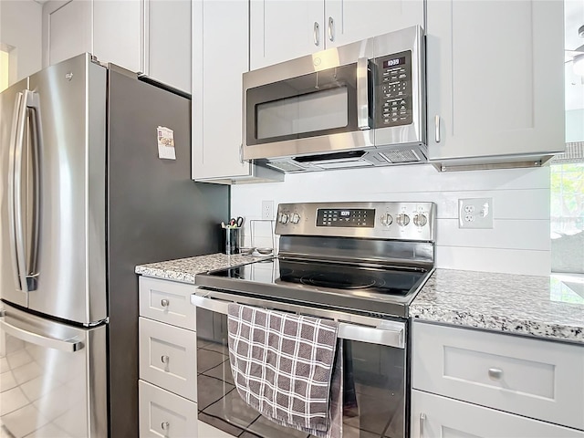 kitchen featuring white cabinetry, stainless steel appliances, light stone countertops, and backsplash