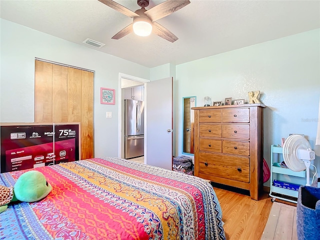 bedroom with light hardwood / wood-style floors, stainless steel refrigerator, and ceiling fan