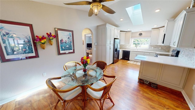 dining space featuring light wood-type flooring, lofted ceiling with skylight, ceiling fan, and sink