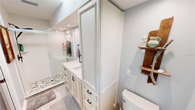 bathroom featuring a tile shower, hardwood / wood-style floors, vanity, and toilet