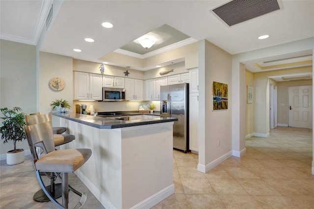 kitchen featuring kitchen peninsula, appliances with stainless steel finishes, crown molding, white cabinetry, and a breakfast bar area