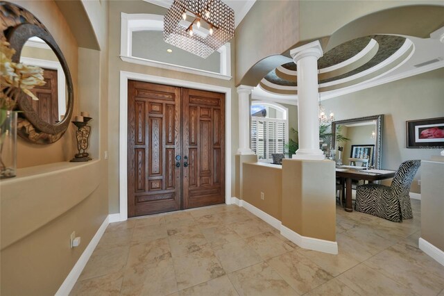 foyer with a chandelier, a high ceiling, decorative columns, and crown molding