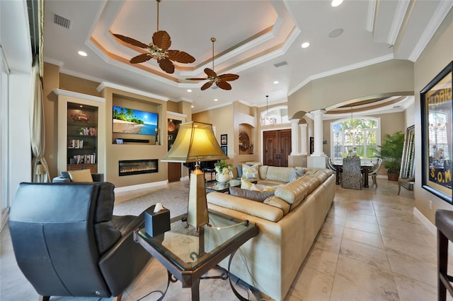 tiled living room featuring ceiling fan with notable chandelier, decorative columns, a tray ceiling, and ornamental molding