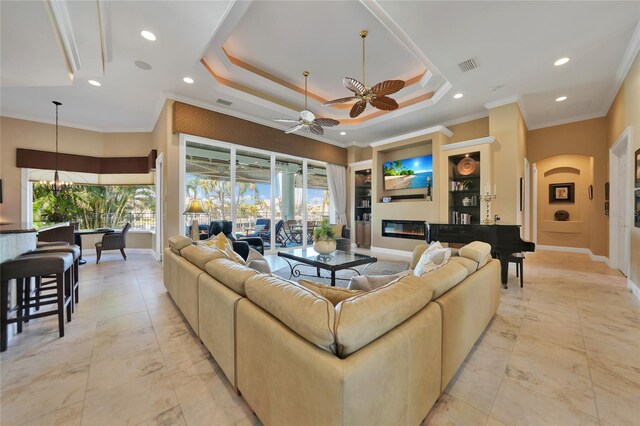 living room with ceiling fan with notable chandelier, crown molding, and a tray ceiling