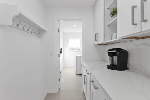 bar with white cabinets, backsplash, and light stone counters