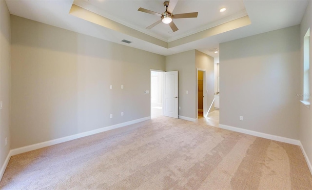 unfurnished room with a tray ceiling, ceiling fan, light colored carpet, and ornamental molding