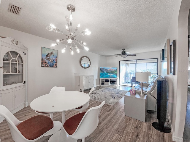 dining space with a textured ceiling, light hardwood / wood-style flooring, and ceiling fan with notable chandelier