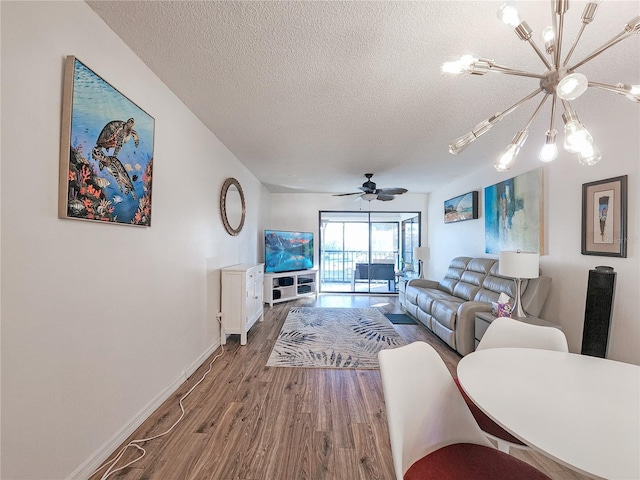 living room featuring ceiling fan with notable chandelier, wood-type flooring, and a textured ceiling