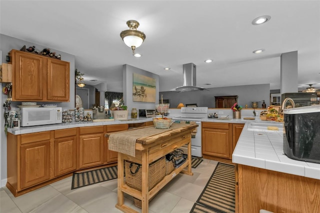 kitchen with tile countertops, wall chimney exhaust hood, white appliances, and kitchen peninsula