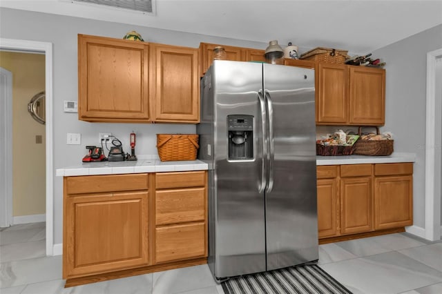 kitchen with tile countertops, light tile patterned floors, and stainless steel refrigerator with ice dispenser