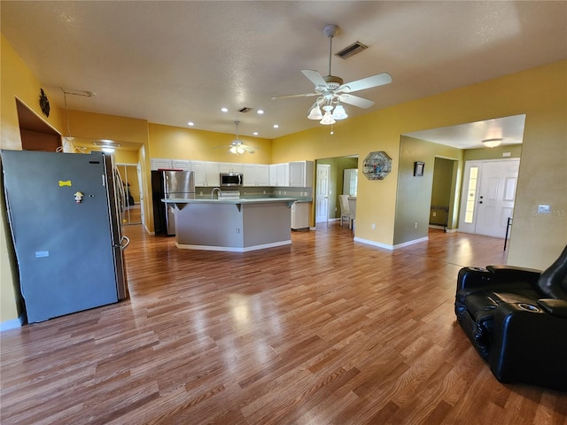 kitchen featuring ceiling fan, stainless steel appliances, light hardwood / wood-style floors, a center island with sink, and white cabinets