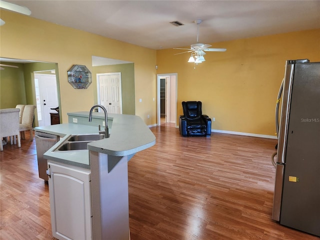 kitchen with light wood-type flooring, stainless steel appliances, ceiling fan, sink, and an island with sink