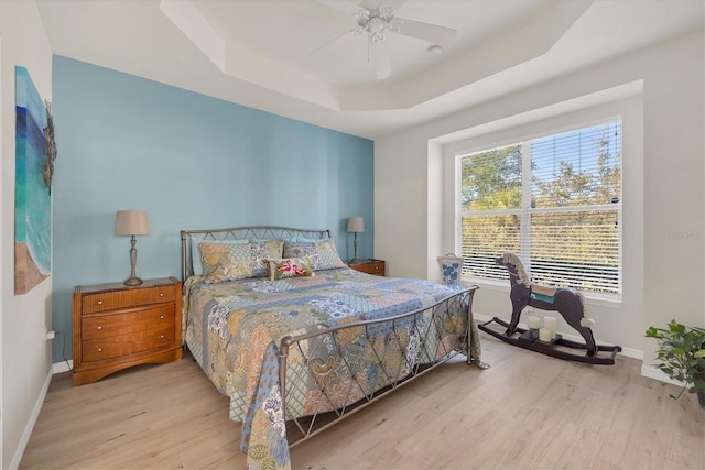 bedroom with light wood-type flooring, a raised ceiling, and ceiling fan