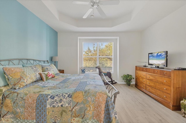 bedroom with a raised ceiling, light hardwood / wood-style flooring, and ceiling fan