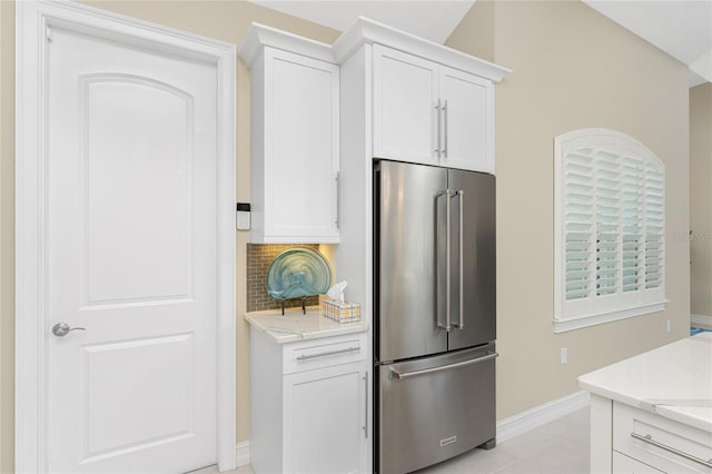 kitchen featuring decorative backsplash, high end refrigerator, white cabinetry, and lofted ceiling