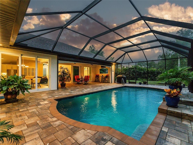 pool at dusk with a bar, a patio, glass enclosure, and area for grilling