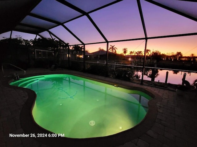 pool at dusk featuring glass enclosure and a patio