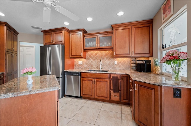 kitchen featuring tasteful backsplash, ceiling fan, sink, stainless steel appliances, and light stone counters